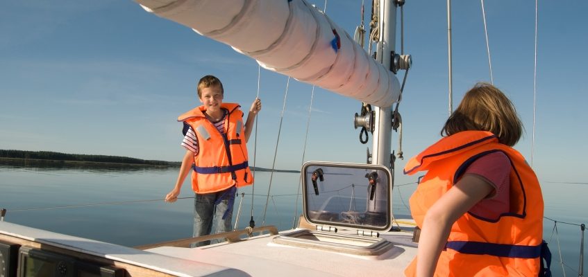children sailing on yatch in orange life jackets