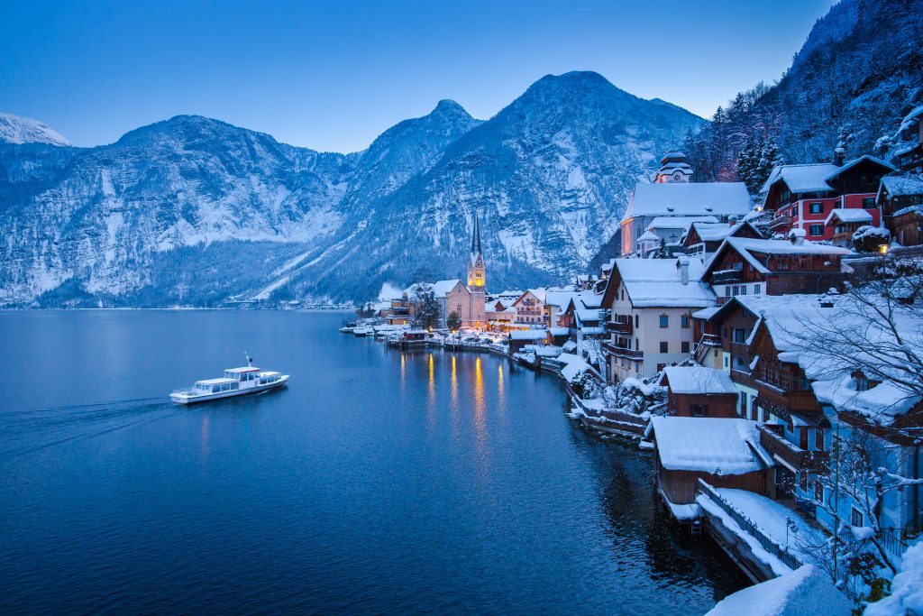 Classic postcard view of famous Hallstatt lakeside town in the Alps with traditional passenger ship on beautiful Hallstattersee in mystical twilight during blue hour in winter, Salzkammergut, Austria