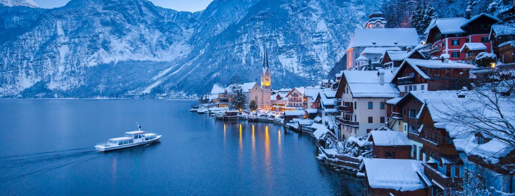 Classic postcard view of famous Hallstatt lakeside town in the Alps with traditional passenger ship on beautiful Hallstattersee in mystical twilight during blue hour in winter, Salzkammergut, Austria