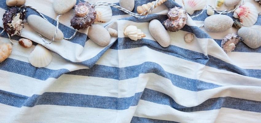 A blue and white striped towel with seashells and rocks