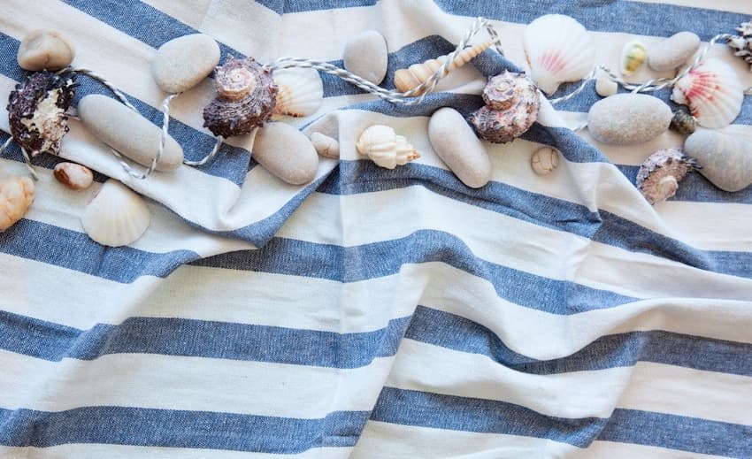 A blue and white striped towel with seashells and rocks